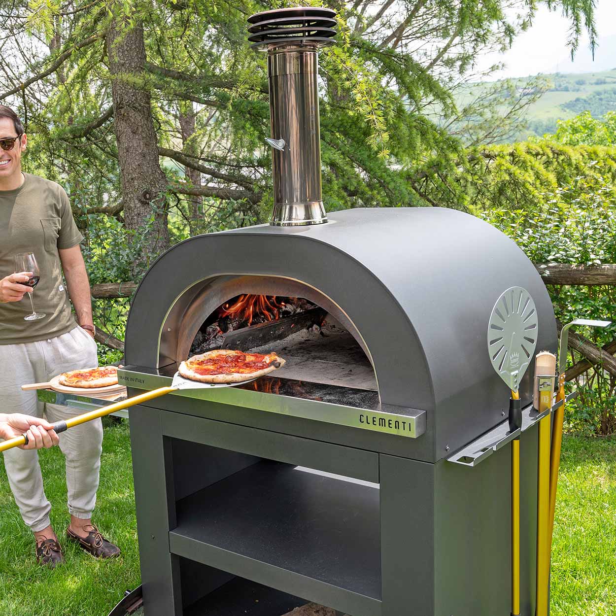 Clementi Gold 100x80 Gas & Wood Fired Pizza Oven Standalone. Lifestyle image shown in Anthracite. Image 6 of 8. From The Outdoor Grill Company.
