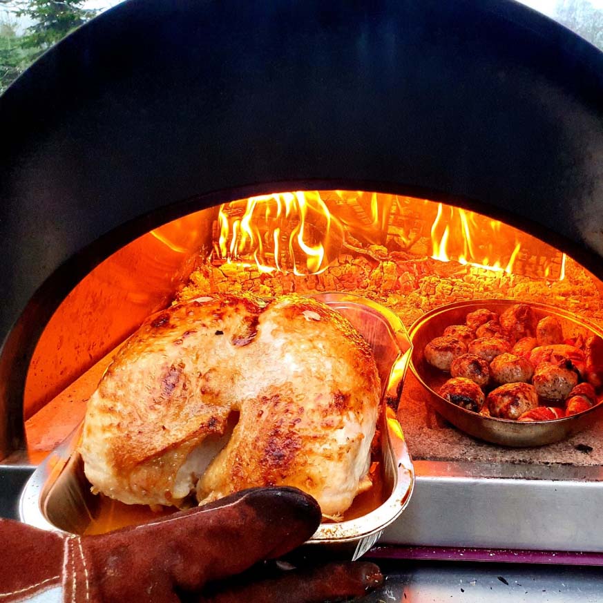 Igneus Classico woodf fired pizza oven all fired up with a roast chicken being put inside for cooking
