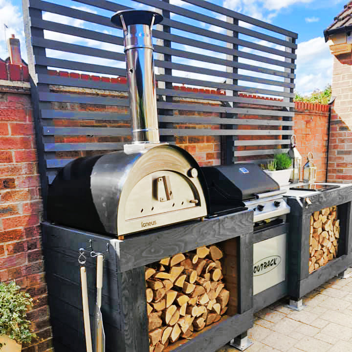 Igneus Classico wood fired oven in black pictured on a black wooden table with logs underneath.