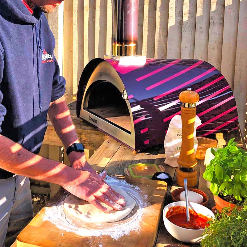 Igneus Classico Wood Fired Pizza Oven in aubergine pictured outside with a man making a pizza base