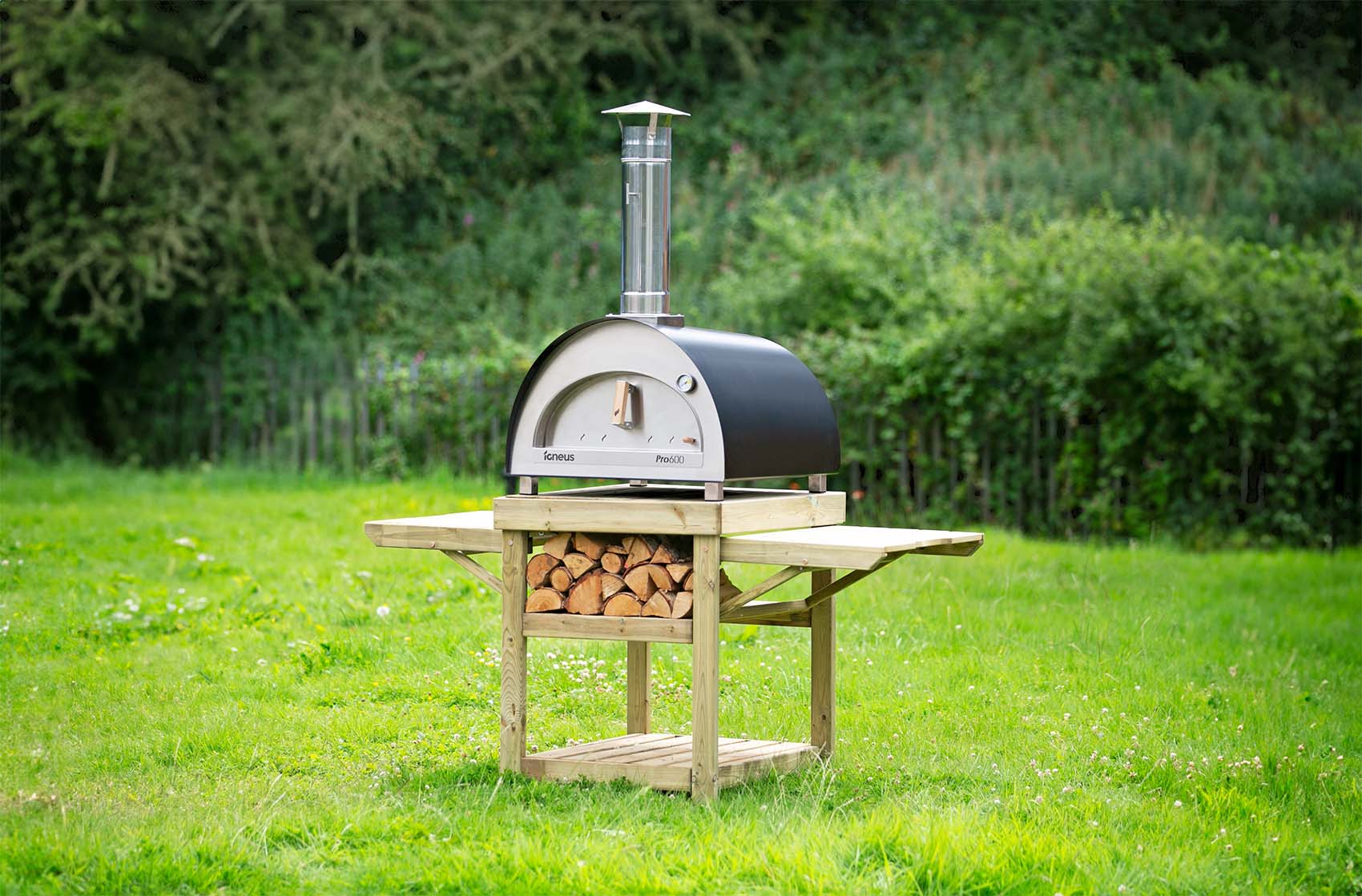 Igneus Pro 600 oven pictured outside on a wooden stand on grass with logs underneath