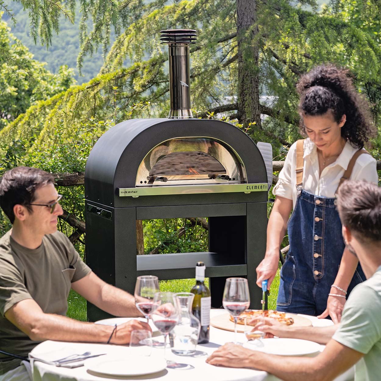 Clementi Gold pizza oven. Lifestyle image with three people shown in anthracite. The Outdoor Grill Company