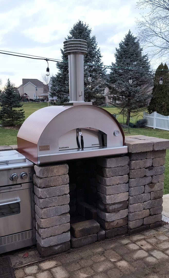 Fontana Forni Mangiafuoco Gas and Wood fired Pizza oven in rosso shown in garden stacked upon a brick base 